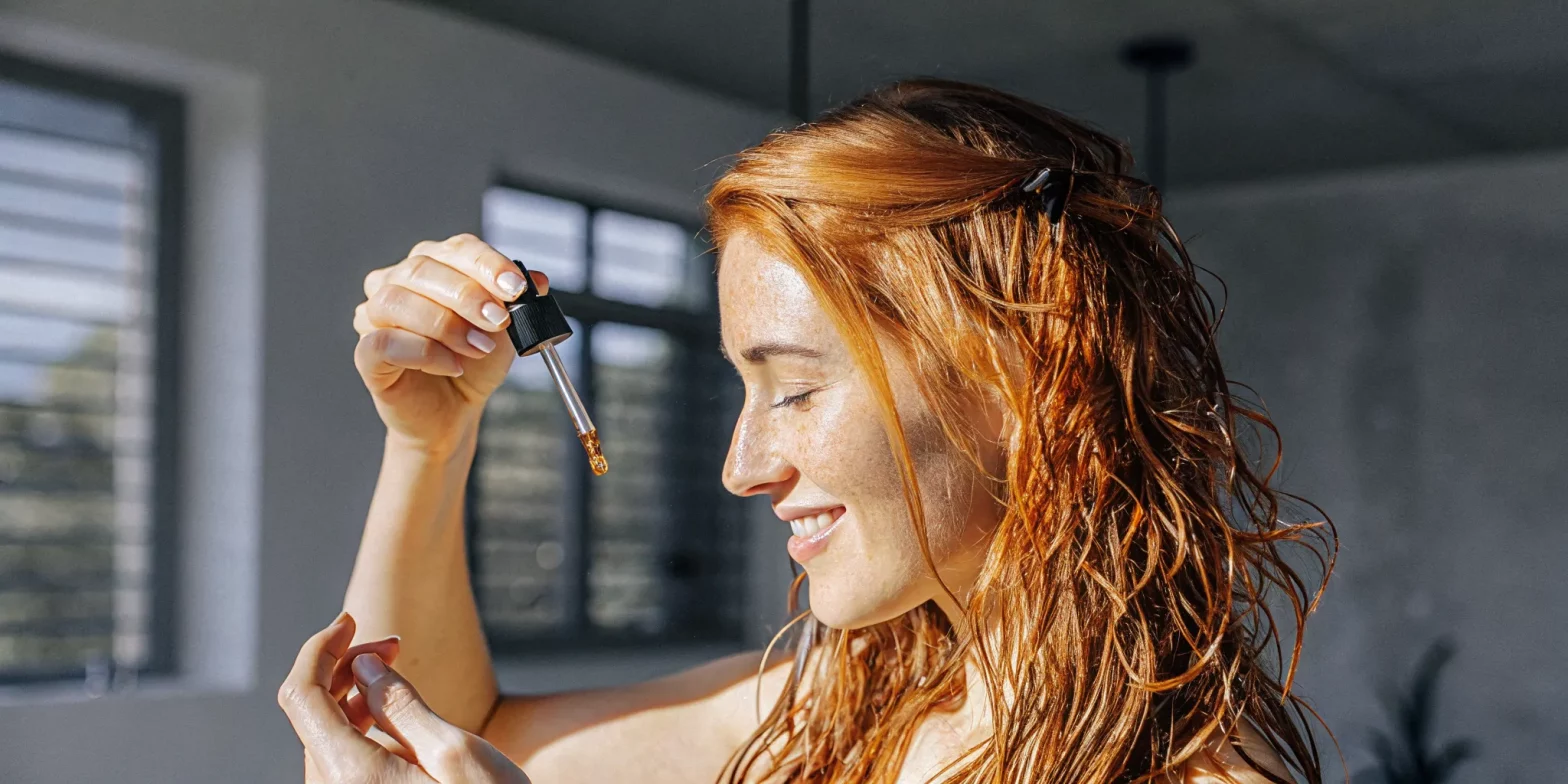 Woman gently applying a few drops of hair oil to the glossy ends of color-treated hair